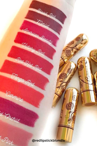 Arm with several swatches of Bésame red lipstick colors next to Bésame lipsticks